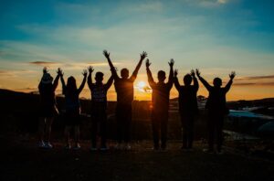 A diverse group of friends raises their arms in celebration against a vibrant sunset backdrop.